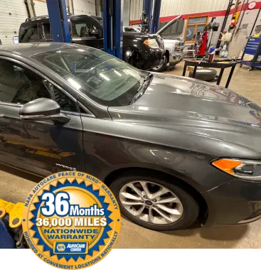 Vehicle inside an auto repair shop with a NAPA AutoCare Center 36-month/36,000-mile nationwide warranty badge in the foreground, highlighting warranty coverage.