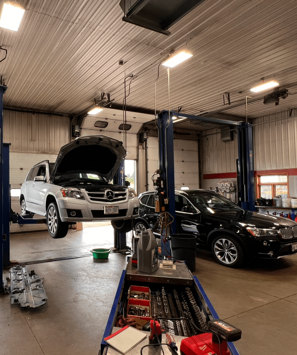 A well-equipped auto repair shop with a white Mercedes-Benz SUV on a lift and a black car next to it, both being serviced.