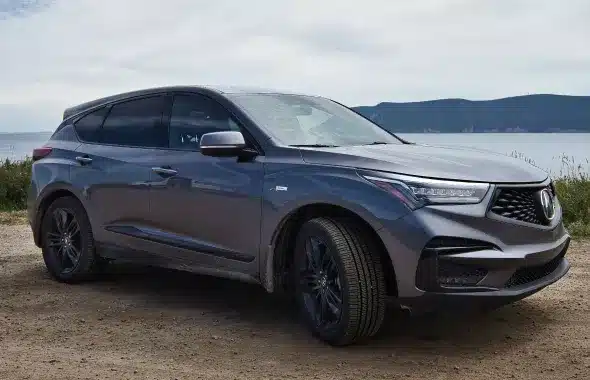 A gray Acura SUV parked by a scenic lakeside with mountains in the background, highlighting its sleek design and performance.