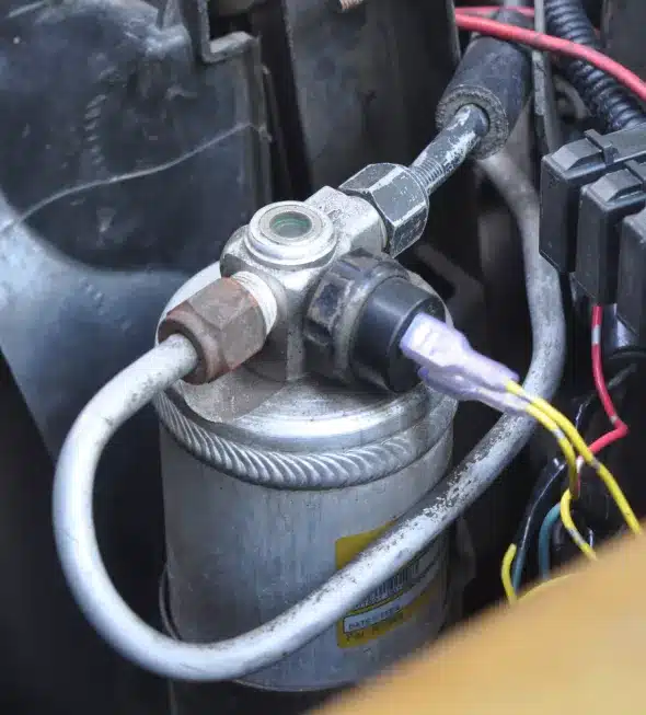 Close-up of an automotive air conditioning compressor, showing detailed connections and wiring in a vehicle's A/C system.