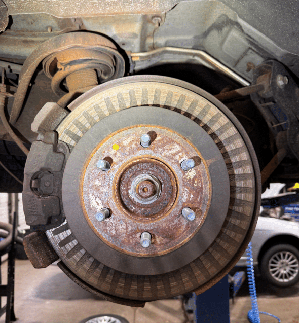 A detailed view of a car's brake rotor and caliper assembly. The image showcases the rusty rotor and the caliper, emphasizing the wear and tear of the braking system.