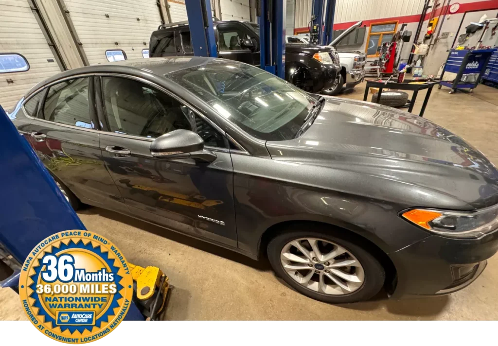 Vehicle inside an auto repair shop with a NAPA AutoCare Center 36-month/36,000-mile nationwide warranty badge in the foreground, highlighting warranty coverage.