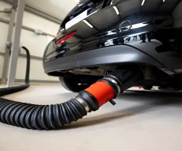 An exhaust emissions testing hose connected to a car's tailpipe. This image underscores the necessity of emissions tests to ensure vehicles comply with environmental regulations and contribute to cleaner air.