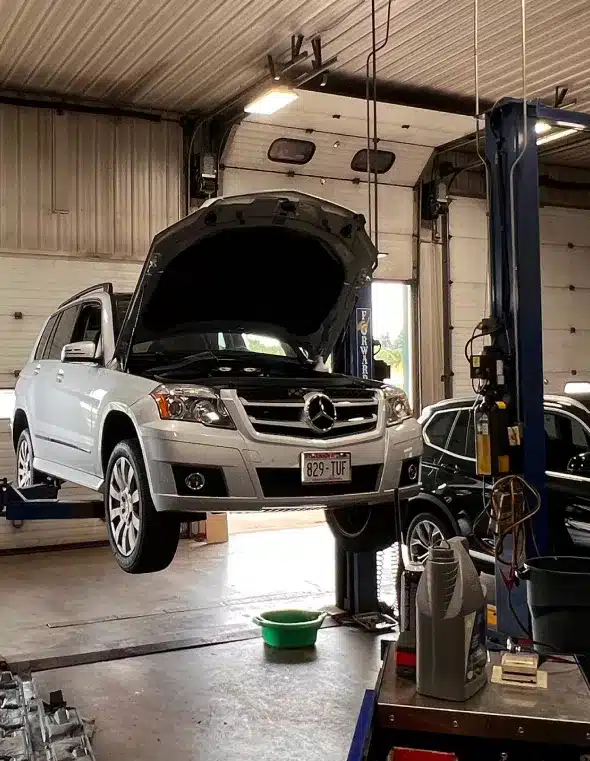 A Mercedes SUV on a lift inside an auto repair shop, with its hood open and ready for service.