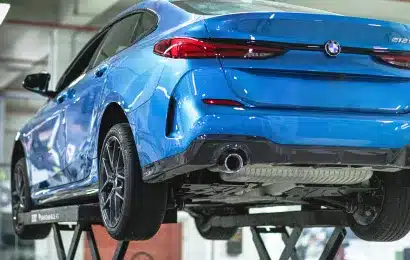 A blue BMW elevated on a hydraulic lift in an auto repair shop, showcasing the underside of the vehicle.