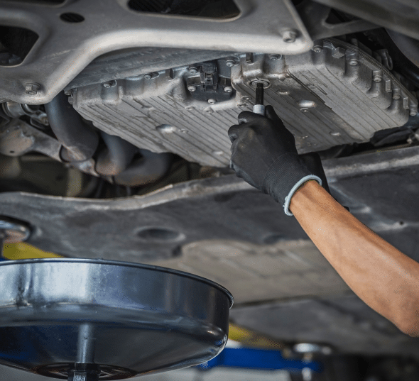 Mechanic performing an oil change on a car, draining old oil from the engine underneath the vehicle.