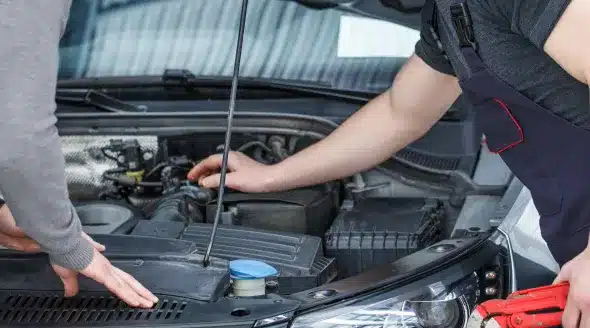 A mechanic using a syringe to extract fluid from a car's reservoir, demonstrating a vital step in pre-trip inspections to ensure proper fluid levels for vehicle safety.