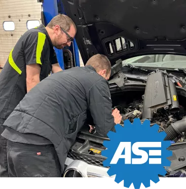 Two ASE-certified technicians working under the hood of a vehicle in an auto repair shop, showcasing their certification and expertise.