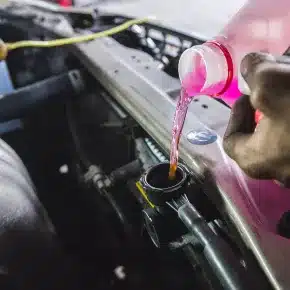 Pouring pink coolant into a car's radiator during a maintenance check. The image underscores the necessity of routine vehicle maintenance to ensure the cooling system functions effectively.