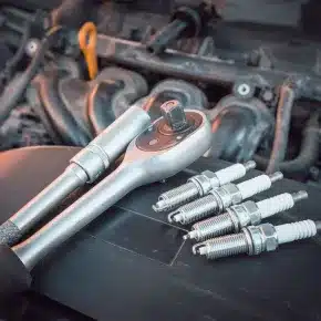 A set of spark plugs and a ratchet wrench placed on an engine cover, highlighting the importance of regular maintenance and replacement of spark plugs for optimal vehicle performance.