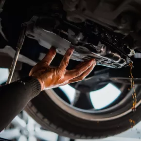 A mechanic's hand draining oil from a vehicle during a maintenance check. The image highlights the importance of regular oil changes in maintaining engine health and performance.