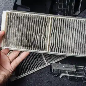 Holding a dirty cabin air filter that needs replacement. The image highlights the importance of regular cabin air filter changes to maintain clean air inside the vehicle and ensure proper ventilation system function.