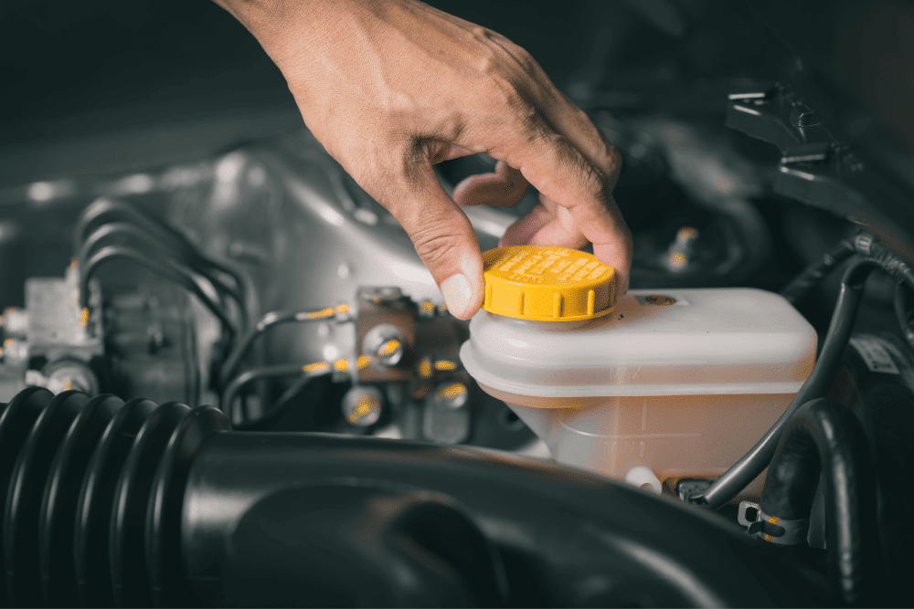 brake fluid flush, auto repair in Sheboygan, WI at NexGen Automotive. Close-up of a hand checking the brake fluid reservoir under the hood of a vehicle.