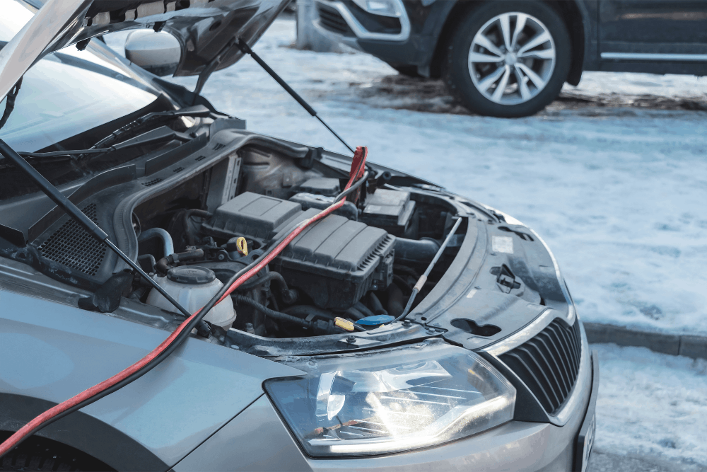 Car battery service, auto repair in Sheboygan, WI by NexGen Automotive. Image of a vehicle with the hood open in winter conditions, connected to jumper cables during professional battery testing and charging to restore reliable starting performance.
