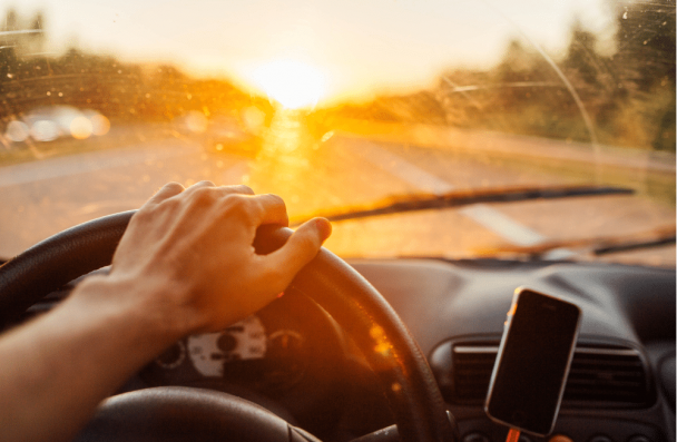 car problems, auto repair in Sheboygan, WI at NexGen Automotive. Interior view of a driver holding the steering wheel during a sunset drive, with warm sunlight streaming through the windshield.
