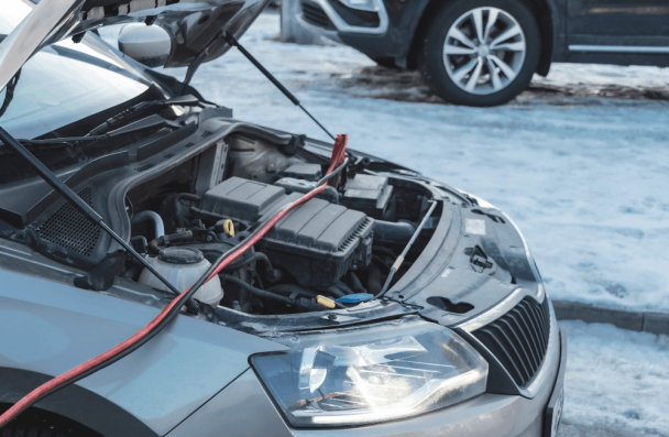 Car battery service, auto repair in Sheboygan, WI by NexGen Automotive. Image of a vehicle with the hood open in winter conditions, connected to jumper cables during professional battery testing and charging to restore reliable starting performance.
